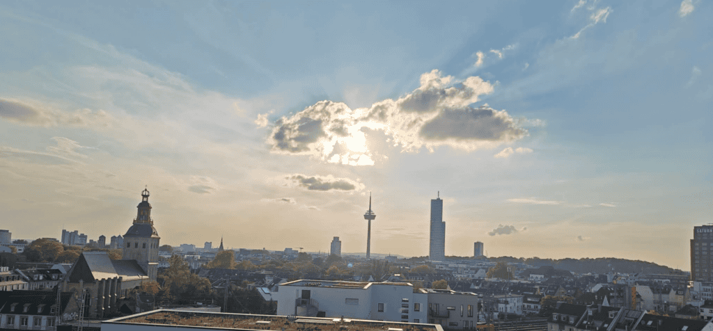 City skyline with a tower, church, and modern buildings under a cloudy sky.